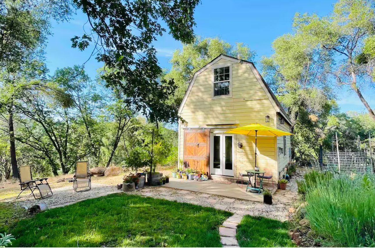 The yellow barn style cottage at Blissful Acres with a sunny patio, lounge chairs and a yellow umbrella